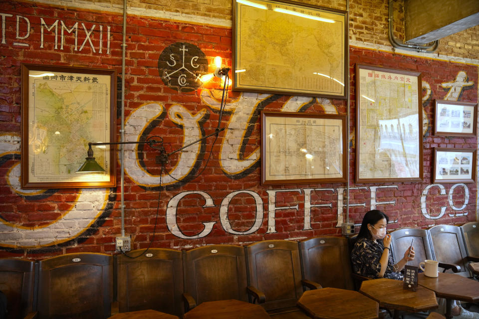 A woman wearing a face mask sits in a cafe in a neighborhood popular with tourists in central Beijing, Tuesday, Aug. 3, 2021. From the Great Wall to the picturesque Kashmir valley, Asia's tourist destinations are looking to domestic visitors to get them through the COVID-19 pandemic's second year. With international travel heavily restricted, foreign tourists can't enter many countries and locals can't get out. The shop's owner said his cafe has felt the effects of tighter restrictions on travel as China worked to contain outbreaks connected to the Delta variant. (AP Photo/Mark Schiefelbein)