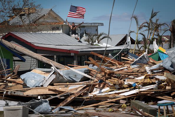 MATLACHA, FLORIDA - SEPTEMBER 30: Whitney Hall waves to a friend from the remains of his home while waving the American flag amidst wreckage left in the wake of Hurricane Ian on the island of Matlacha on September 30, 2022 in Matlacha, Florida. The hurricane brought high winds, storm surge and rain to the area causing severe damage. (Photo by Win McNamee/Getty Images)