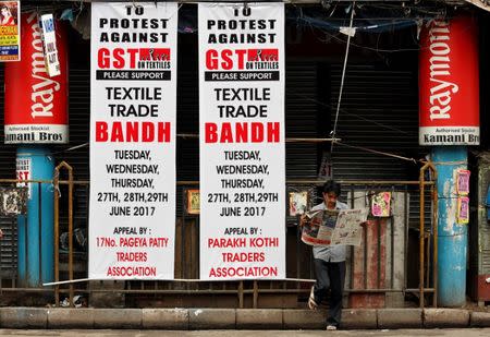 A man reads a news paper next to banners in front of closed garments market during a protest against implementation of Goods and Services Tax (GST) on textiles, in Kolkata, India, June 29, 2017. REUTERS/Rupak De Chowdhuri