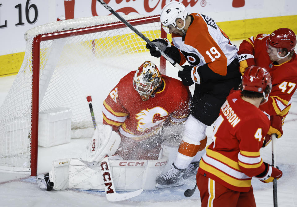 Philadelphia Flyers forward Garnet Hathaway (19) is checked by Calgary Flames forward Connor Zary, top right, into Flames goalie Jacob Markstrom during second-period NHL hockey game action in Calgary, Alberta, Sunday, Dec. 31, 2023. (Jeff McIntosh/The Canadian Press via AP)