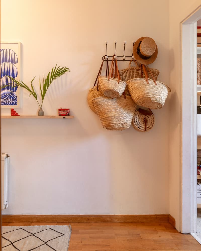 white entryway with baskets hanging on pegs and wood floating shelf