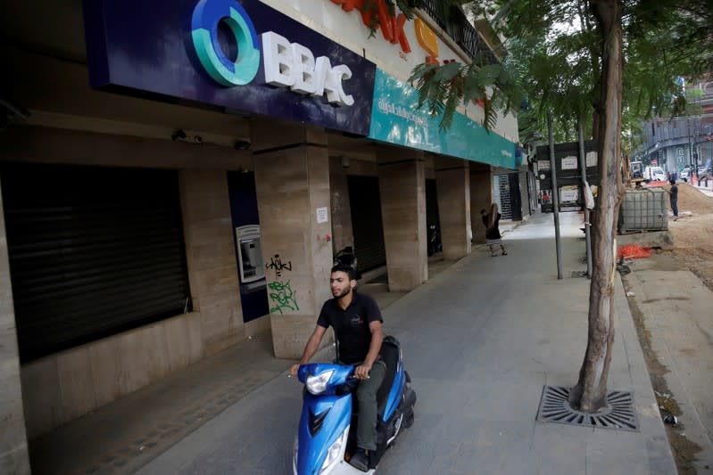A man drives a motorbike past a closed bank office in Beirut
