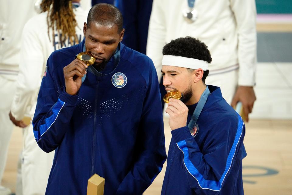 U.S. guards Kevin Durant (7) and Devin Booker (15) celebrate with their gold medals on the podium after defeating France in the men's basketball gold medal game during the 2024 Summer Olympics in Paris, Saturday, August 10, 2024, at Accor Arena.