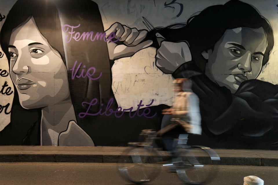 FILE - A man rides bicycle front of a mural signed by Clacks-one and Heartcraft_Street art, depicting women cutting their hair to show support for Iranian protesters standing up to their leadership over the death of a young woman in police custody, in a tunnel in Paris, France, Wednesday, Oct. 5, 2022. As anti-government protests roil cities and towns in Iran for a fourth week, sparked by the death of a 22-year-old woman detained by Iran's morality police, tens of thousands of Iranians living abroad have marched on the streets of Europe, North America and beyond in support of what many believe to be a watershed moment for their home country. (AP Photo/Francois Mori, File)