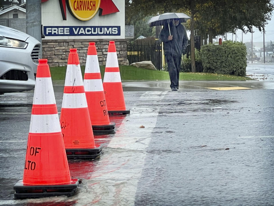 Larry Bernard Smith is protected from the rain as he crosses Foothill Blvd. on his way to get breakfast in Rialto, Calif., on Tuesday, Nov. 8, 2022. The westbound lanes of Foothill Blvd. are closed due to flooding. (Eric Vilchis/The Orange County Register via AP)