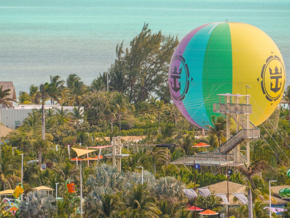 The hot air balloon on CocoCay from above with palm trees surrounding it and clear ocean waters in the background