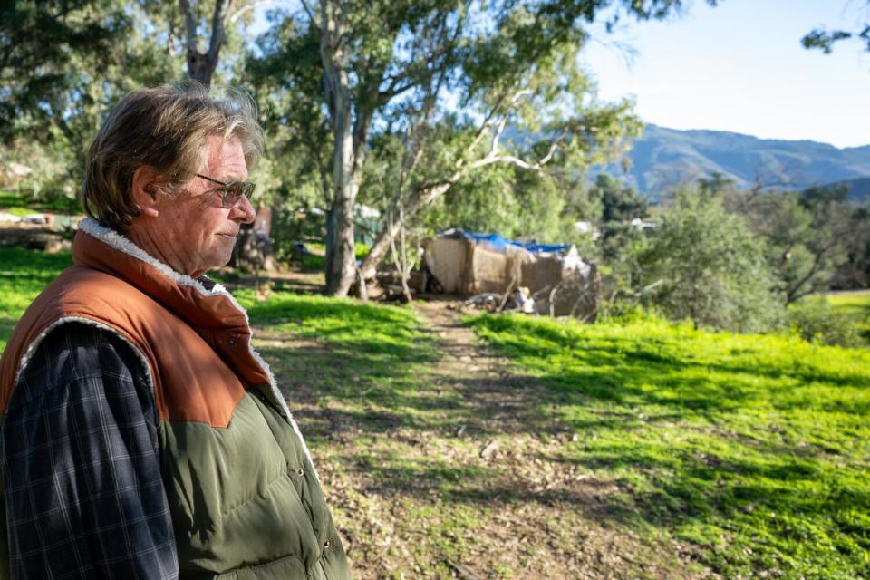 A man surveys a grassy homeless camp with mountains in the distance.