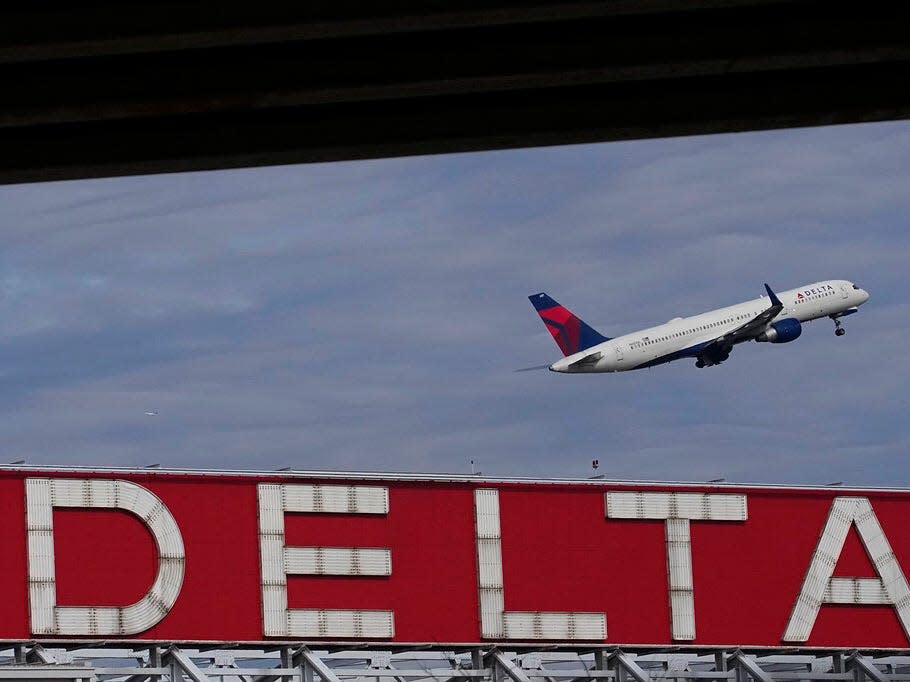 Delta plane taking off against a cloudy sky and a red sign with Delta written in white capital letters on it.