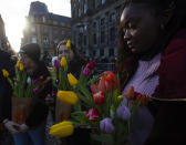 Three women watch scores of people pick free tulips on Dam Square in front of the Royal Palace in Amsterdam, Netherlands, Saturday, Jan. 18, 2020, on national tulip day which marks the opening of the 2020 tulip season. (AP Photo/Peter Dejong)