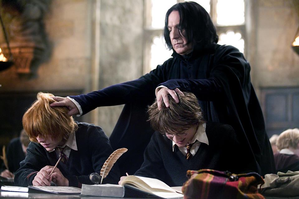 Severus Snape stands behind Ron Weasley and Harry Potter in a classroom situation and puts his hand on their heads