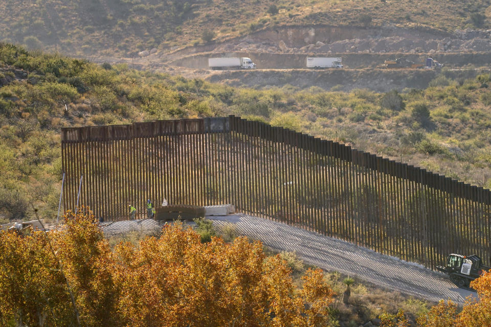 Trucks drive along Mexico's Route 2, top, as border wall construction continues along a cleared pathway, Wednesday, Dec. 9, 2020, in Guadalupe Canyon, Ariz. Crews have been dynamiting remote and rugged mountainsides in the southeast corner of Arizona, reshaping the landscape in an effort to build more border wall before President Trump's term ends in January. Construction of the border wall, mostly in government owned wildlife refuges and Indigenous territory, has led to environmental damage and the scarring of unique desert and mountain landscapes that conservationists fear could be irreversible. (AP Photo/Matt York)