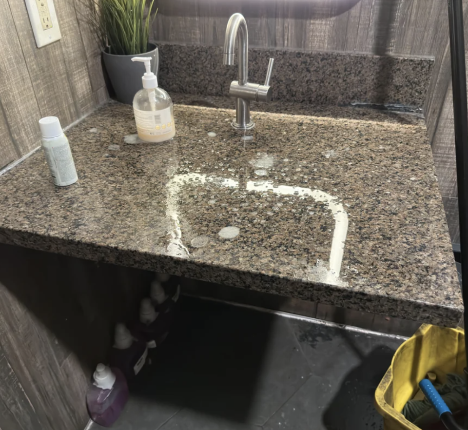 Kitchen sink with residue forming a smiley face on granite countertop, cleaning supplies nearby