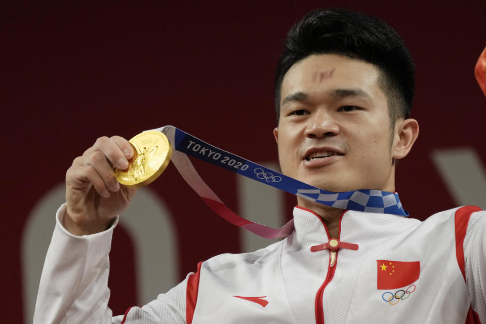 Shi Zhiyong of China celebrates on the podium after winning the gold medal in the men's 73kg weightlifting event, at the 2020 Summer Olympics, Wednesday, July 28, 2021, in Tokyo, Japan. (AP Photo/Luca Bruno)
