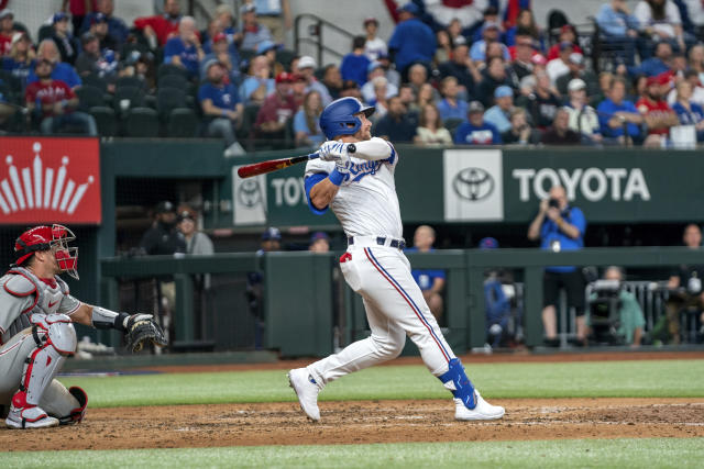 Texas Rangers' Robbie Grossman, right, follows through on a three-run home run that scored Josh Jung and Jonah Heim during the fourth inning of an opening day baseball game against the Philadelphia Phillies, Thursday, March 30, 2023, in Arlington, Texas. (AP Photo/Jeffrey McWhorter)