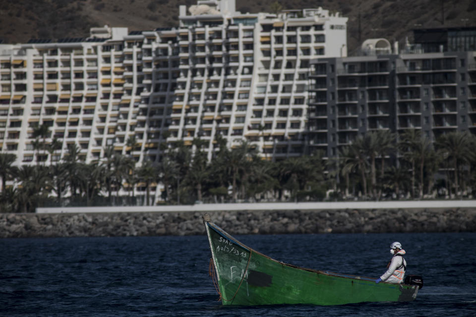 A member of Spanish Coastguards guides a boat used by migrants at as they arrive in Arguineguin port carrying migrants after their rescue in Gran Canaria island, Spain on Wednesday Nov. 25, 2020. Spanish rescue services said Wednesday at least seven people died after a migrant boat carrying more than 30 people hit rocks close to a small port on the Canary Island of Lanzarote. Many of the rescued were taken to the Arguineguín dock on the southwestern coast of Gran Canaria island, where several thousand people of different origin are being kept, some in tents. (AP Photo/Javier Fergo)