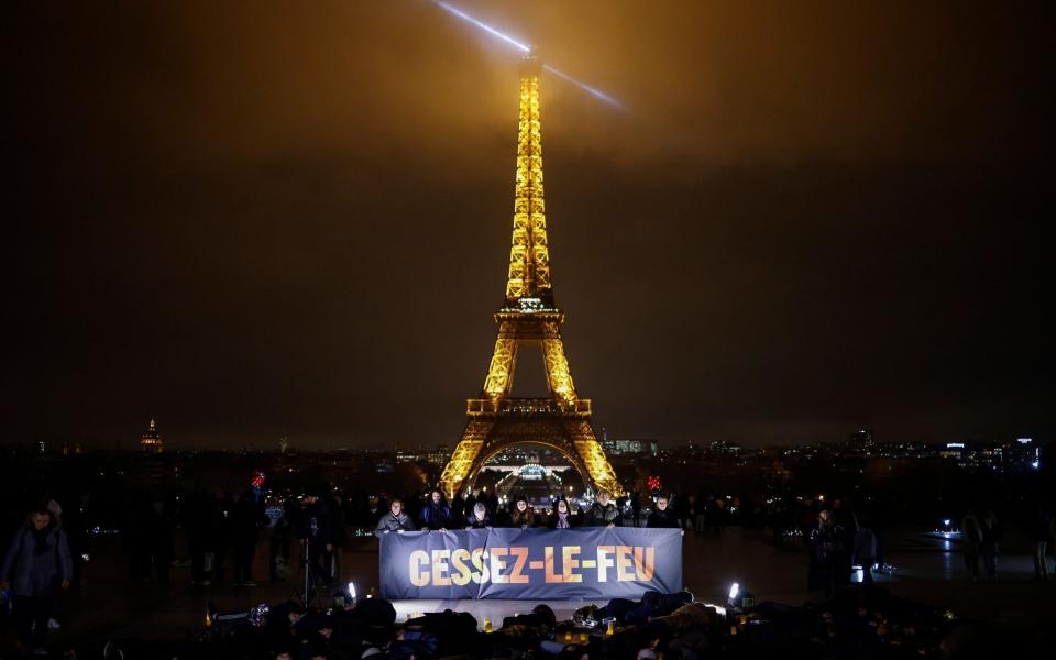 People pose with a banner reading 'Ceasefire' in front of the illuminated Eiffel Tower