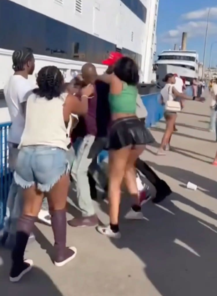 Several men and women can be seen pushing and shoving each other on the pier right next to the massive yacht. Supplied