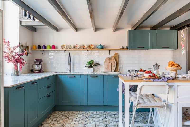 A kitchen with white tiled backsplash and teal cabinets.