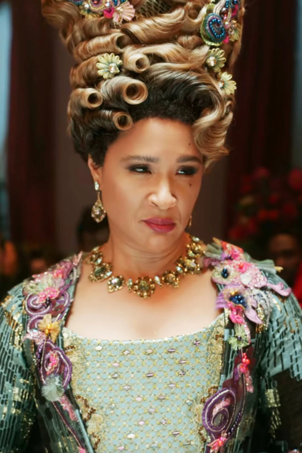 Golda Rosheuvel as Queen Charlotte in a regal gown with an elaborate and tall hairstyle along with detailed jewelry in a scene from the TV show 