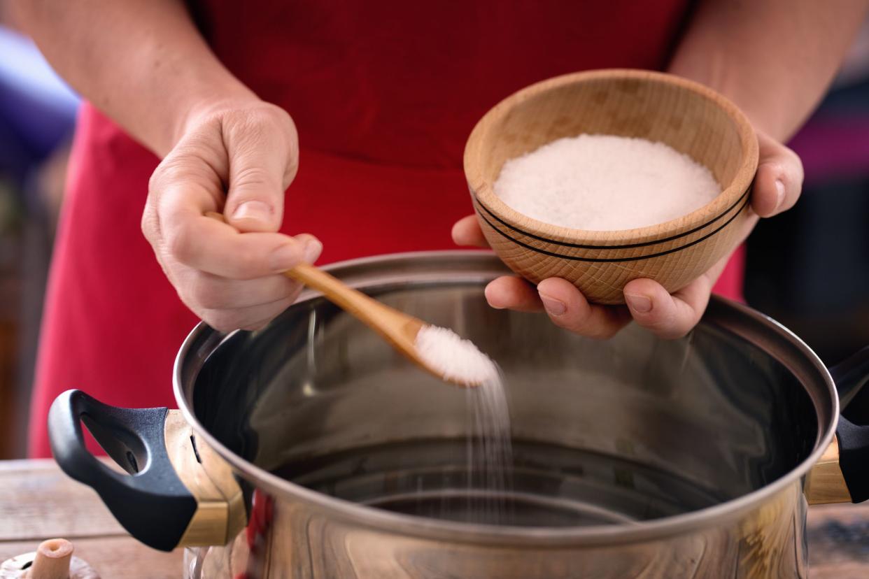 Pasta cooking - Hands holding wood bowl with salt, seasoning water with sea salt.