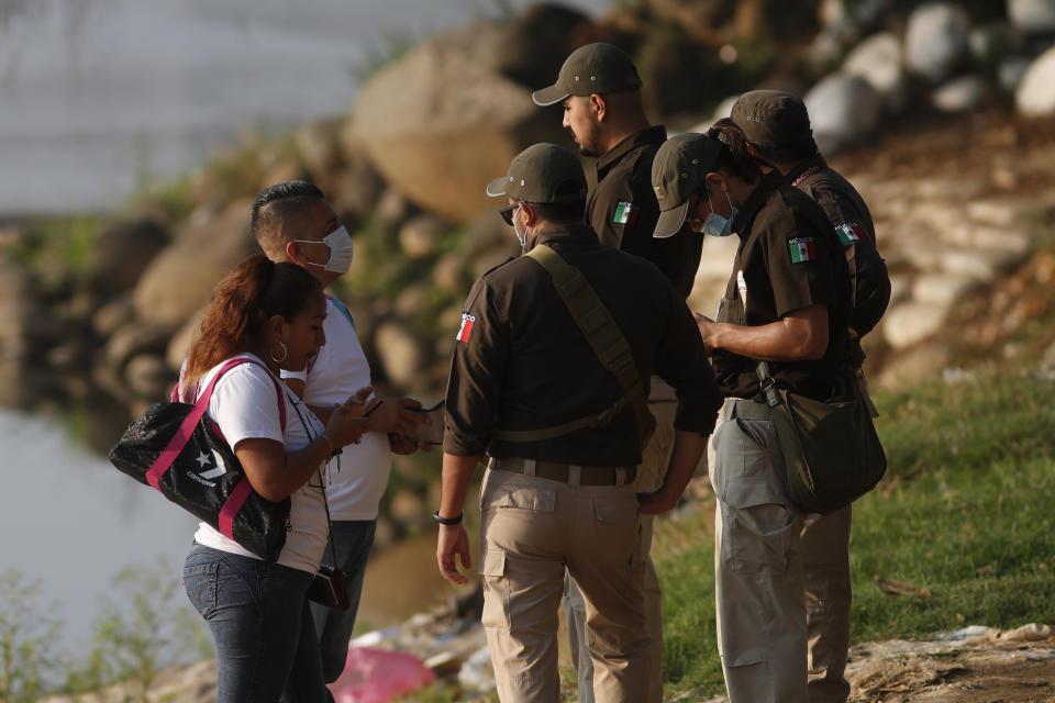 Mexican immigration agents review the IDs of Guatemalan travelers at an access point to the Suchiate River, the natural border between Guatemala and Mexico, near Ciudad Hidalgo, Mexico, Sunday, March 21, 2021. Mexico sent hundreds of immigration agents, police and National Guard to its southern border to launch an operation to crack down on migrant smuggling. (AP Photo/Eduardo Verdugo)