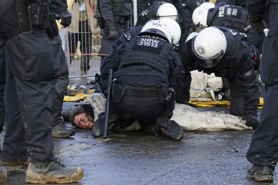 A protester writhes in pain as she’s pinned down by police officers trying to clear a blocked road at the Luetzerath village near Erkelenz, Germany, Wednesday, Jan. 11, 2023. Police in riot gear began evicting climate activists Wednesday from the condemned village that is due to be demolished for the expansion of a coal mine. (AP Photo/Frank Jordans)