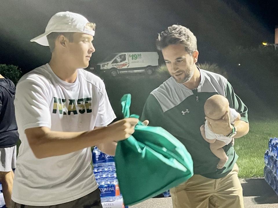 Nease lacrosse coach Max Gurowski holds his 13-week old son Myles while helping Zac Atotea load bags of food during the 11th annual Hope for the Holidays event at the TPC Sawgrass.
