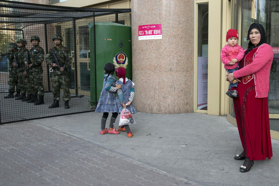 FILE - Uighur children play near a cage protecting heavily armed Chinese paramilitary policemen on duty in Urumqi in northwest China's Xinjiang Uyghur Autonomous Region on May 1, 2014. As Beijing prepares to hold the Winter Olympics opening in February 2022, China's president and party leader Xi Jinping appears firmly in control. The party has made political stability paramount and says that has been the foundation for the economic growth that has bettered lives and put the nation on a path to becoming a regional if not global power. (AP Photo/Ng Han Guan, File)