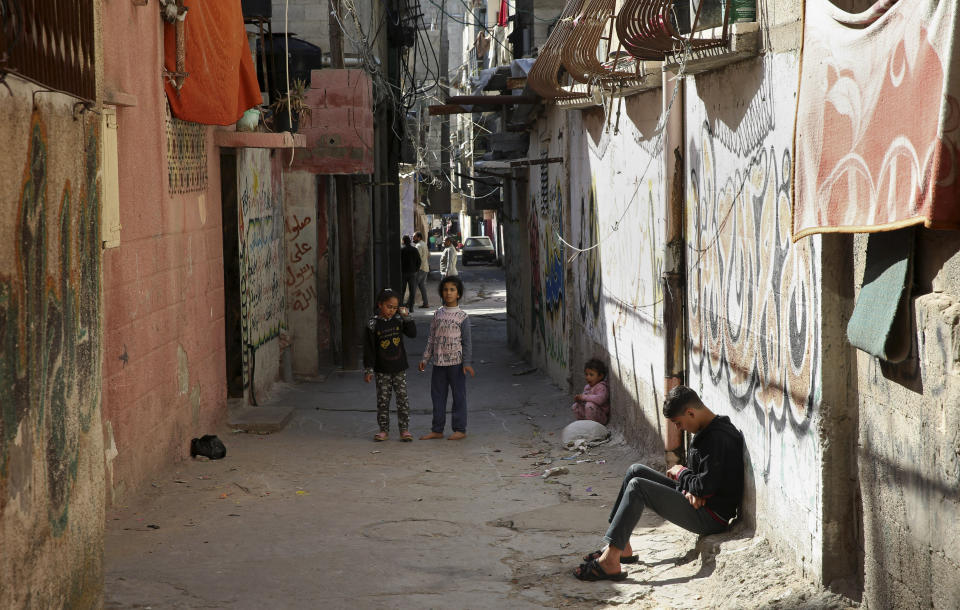 In this April 21, 2019 photo, a Palestinian teenager sits in an alley as children play in front of their family house, in the Shati refugee camp, in Gaza City. The blockade Israel and Egypt imposed on Gaza after the Hamas militant group took power in 2007 has ravaged the economy. The skyrocketing unemployment rates, combined with foreign aid cuts and Hamas' mismanagement, has left thousands of families dependent on food aid and social welfare. Many young Gazans have been forced to put off their dreams of marriage because they cannot afford it. (AP Photo/Adel Hana)