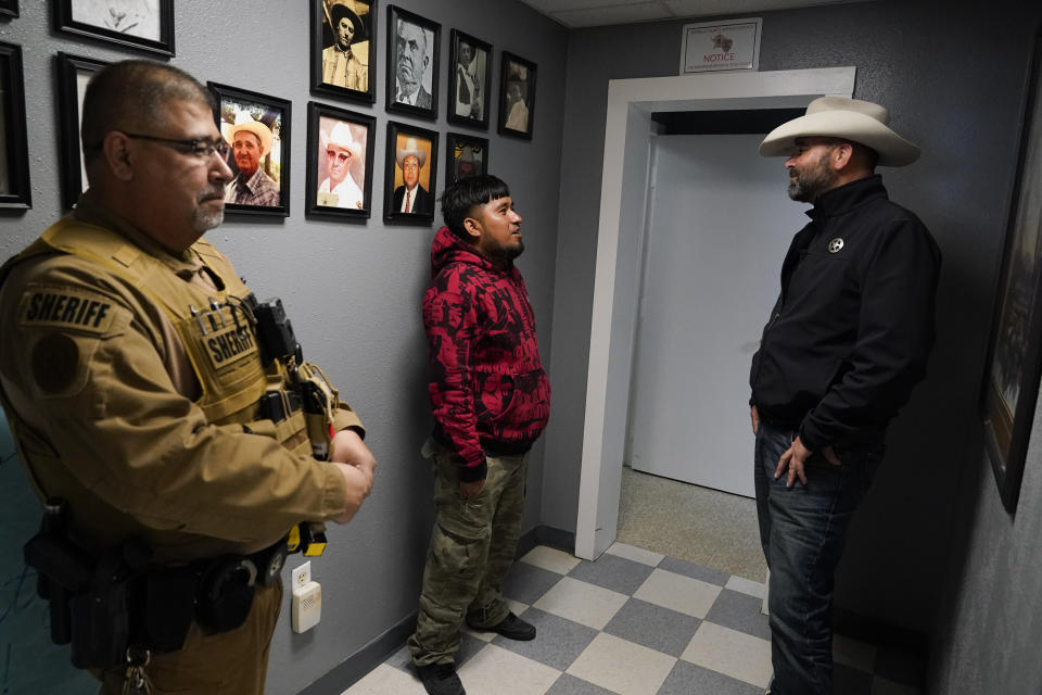 Terrell County Sheriff Thaddeus Cleveland, right, speaks to a recently detained migrant from Mexico, as Sgt. Manuel Jimenez looks on, at the Terrell County Sheriff's Office, Thursday, March 21, 2024, in Sanderson, Texas. (AP Photo/Erik Verduzco)