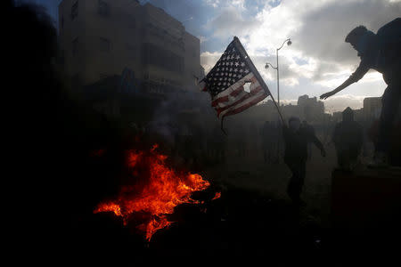 A Palestinian protester prepares to burn a U.S. flag during clashes with Israeli troops at a protest against U.S. President Donald Trump's decision to recognize Jerusalem as the capital of Israel, near the Jewish settlement of Beit El, near the West Bank city of Ramallah December 7, 2017. REUTERS/Mohamad Torokman