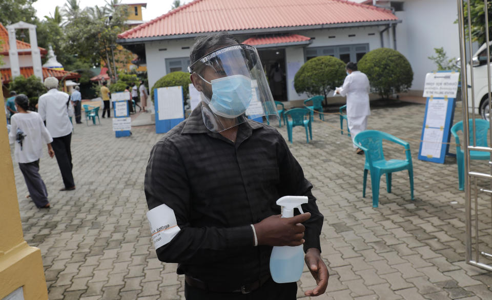 A Sri Lankan polling officer wearing mask and face shield stands holding a sanitizer sprayer at the entrance to a polling center during the parliamentary election in Colombo, Sri Lanka, Wednesday, Aug. 5, 2020. The election was originally scheduled for April but was twice postponed due to the COVID-19 pandemic. (AP Photo/Eranga Jayawardena)