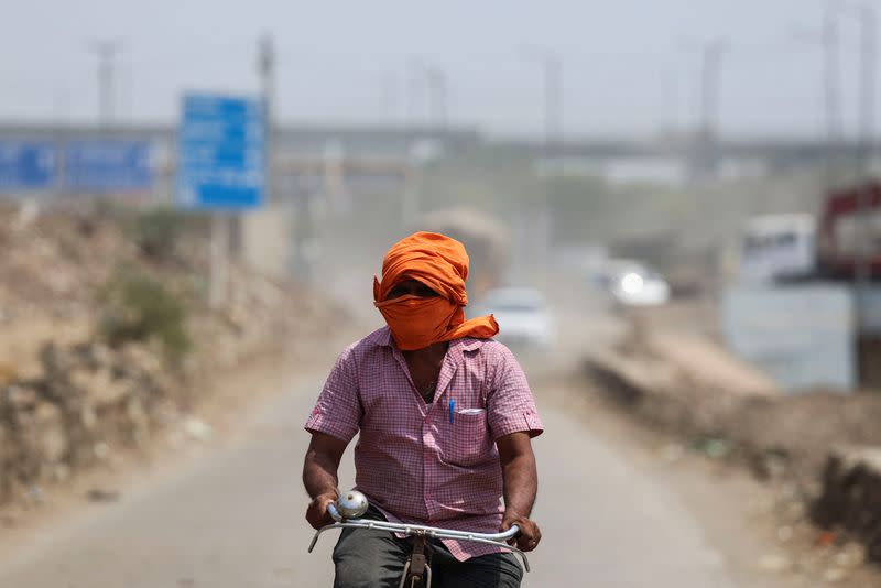 A man rides his cycle near a landfill site on a hot summer day during a heatwave in New Delhi