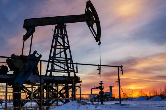 An oil pump with the sun in the background and snow on the ground.