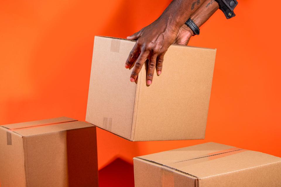 Hands stack cardboard boxes in front of an orange background.