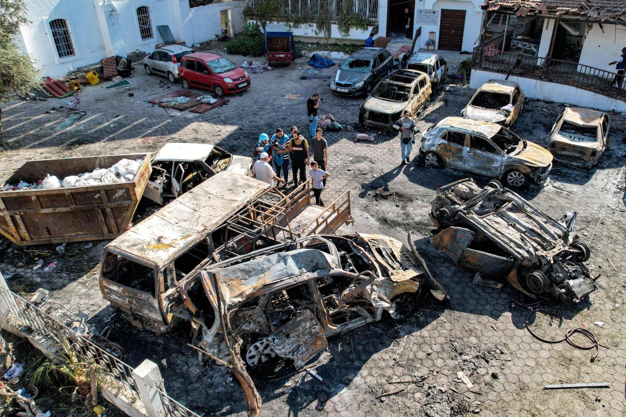 People standing before destroyed buildings and burned-out cars in the parking lot outside Ahli Arab hospital.