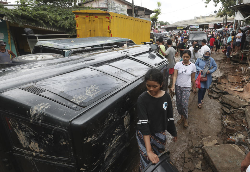 Residents walk near the wreckage of cars that were swept away by flood in Bekasi, West Java, Indonesia, Friday, Jan. 3, 2020.Severe flooding in greater Jakarta has killed scores of people and displaced tens of thousands others, the country's disaster management agency said. (AP Photo/Achmad Ibrahim)