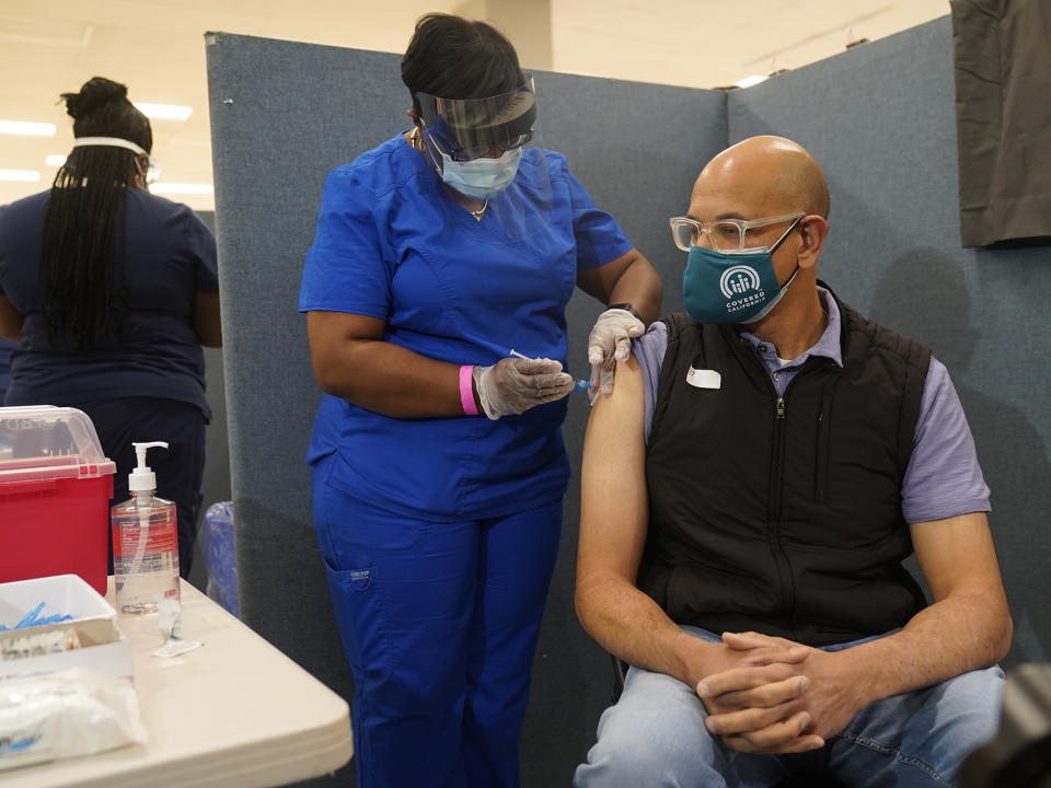 Licensed vocational nurse LeShay Brown, middle, inoculates Dr. Mark Ghaly, Secretary, California Health and Human Services, right, at the Baldwin Hills Crenshaw Plaza in Los Angeles Thursday, March 11, 2021. Ghaly was vaccinated with the new one-dose Janssen COVID-19 vaccine by Johnson & Johnson. (AP Photo/Damian Dovarganes)