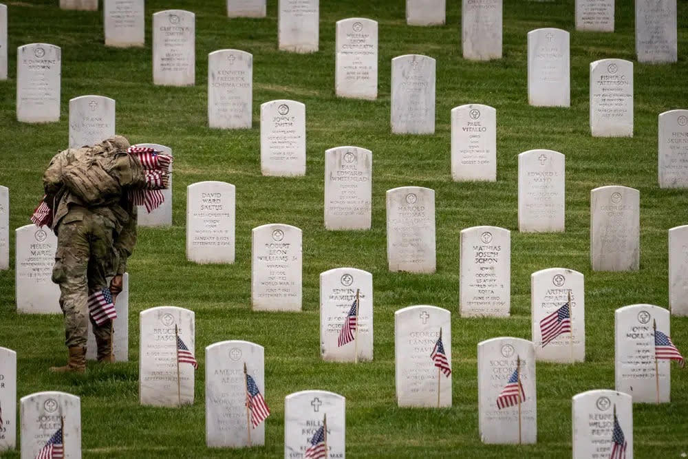 A member of the 3rd U.S. Infantry Regiment also known as The Old Guard, places flags in front of each headstone for “Flags-In” at Arlington National Cemetery in Arlington, Thursday, May 25, 2023, to honor the Nation’s fallen military heroes ahead of Memorial Day. (AP Photo/Andrew Harnik)