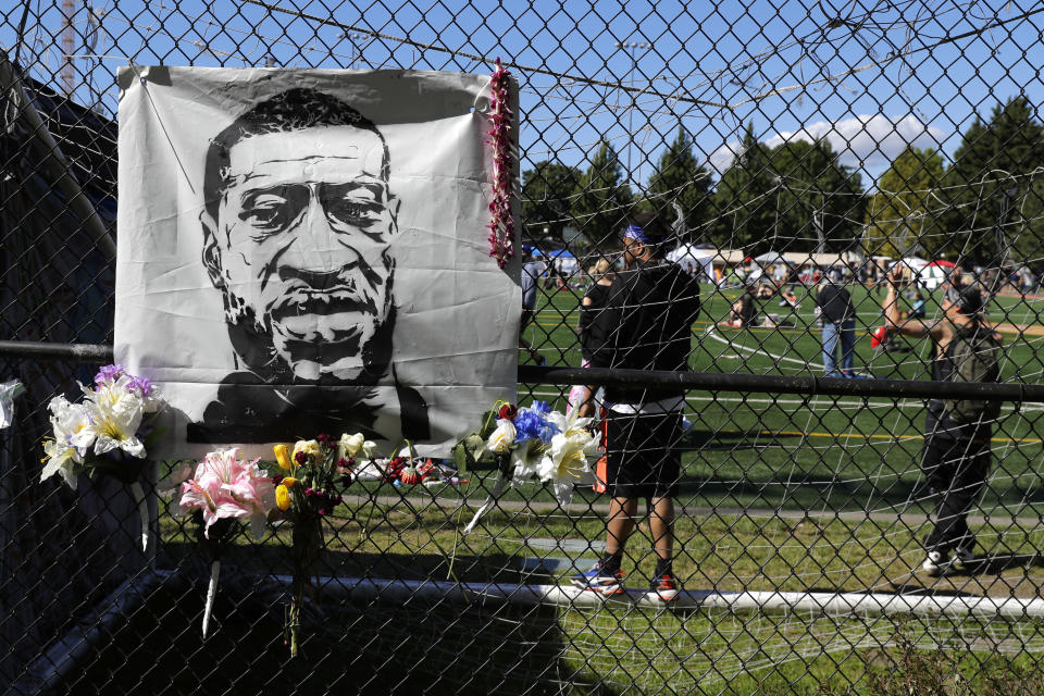 Flowers are placed next to an image of George Floyd on a fence surrounding Cal Anderson Park, Wednesday, June 17, 2020, inside what has been named the Capitol Hill Occupied Protest zone in Seattle. Police pulled back from several blocks of the city's Capitol Hill neighborhood near the Police Department's East Precinct building earlier in the month after clashes with people protesting the police killing of Floyd in Minneapolis. (AP Photo/Ted S. Warren)