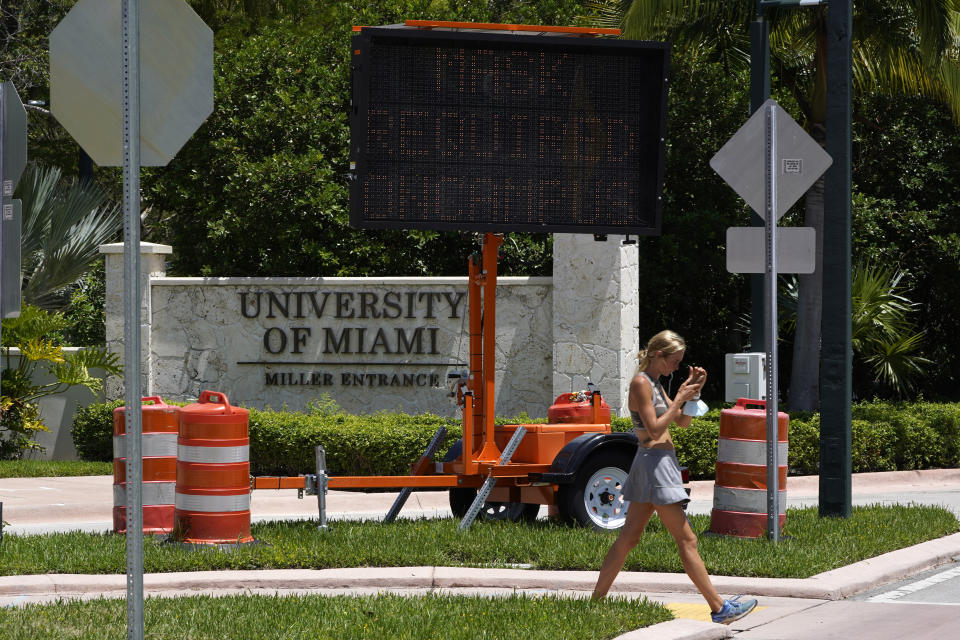 FILE - In this Aug. 25, 2020, file photo, a pedestrian walks past a sign stating that masks, used to prevent the spread of COVID-19, are required to be worn on campus, by an entrance to the University of Miami in Coral Gables, Fla. As more and more schools and businesses around the country get the OK to reopen, some college towns are moving in the opposite direction because of too much partying and too many COVID-19 infections among students. (AP Photo/Wilfredo Lee, File)