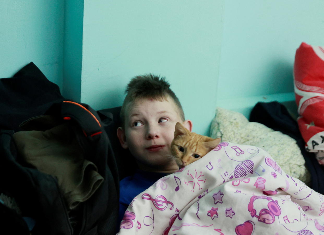 A child and a cat lie under a blanket in a school basement.