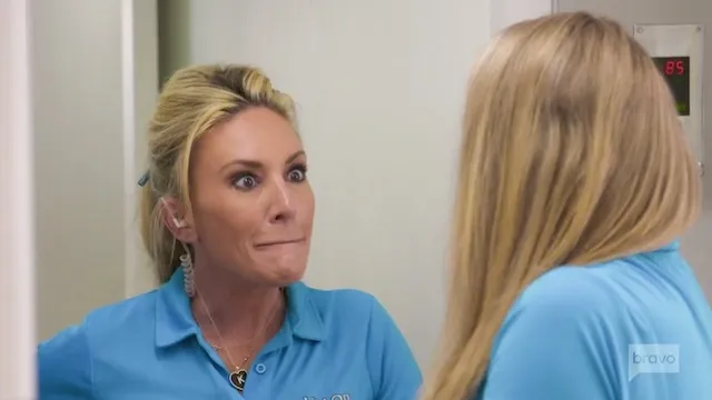 Two women in blue uniforms having an intense conversation on a ship. One has her hair tied back, looking surprised; the other has long blonde hair facing away