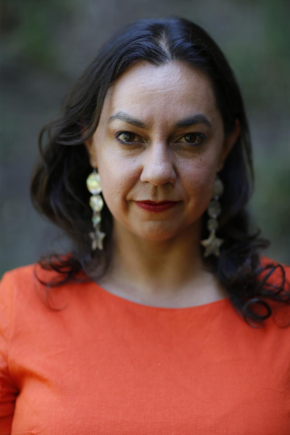 A woman in an orange dress and abalone shell earrings faces the camera.