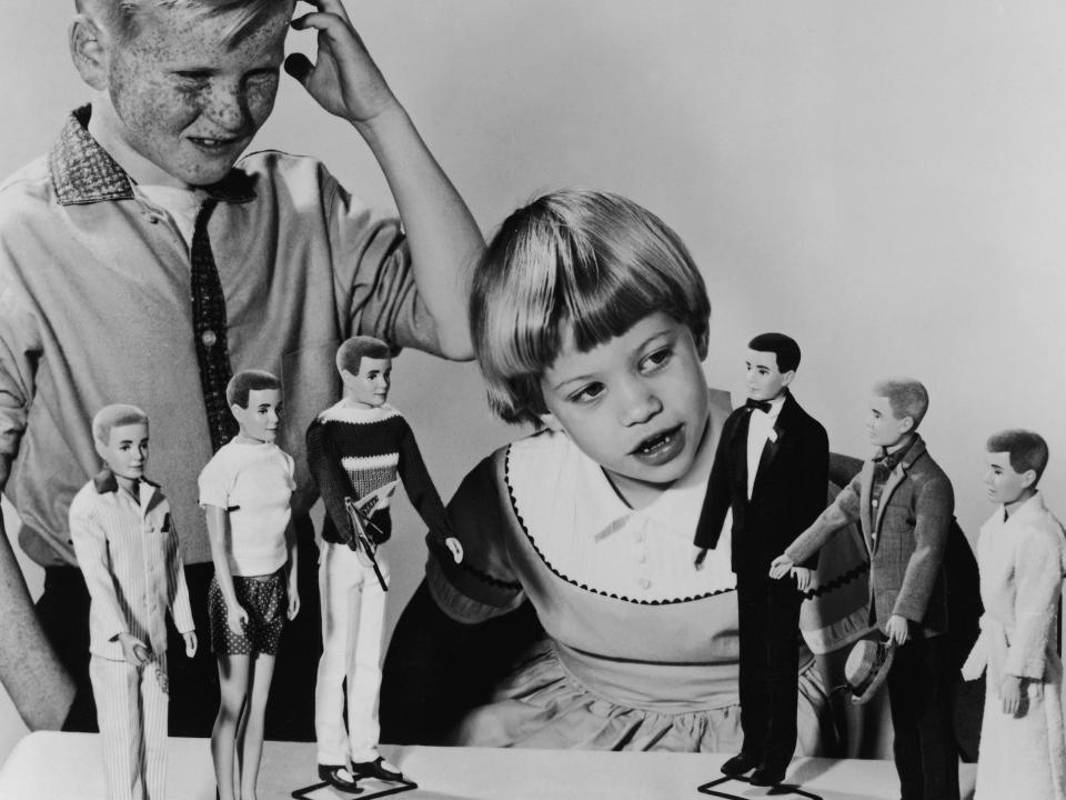 A young boy looks confused while a young girl inspects Ken dolls in 1961.