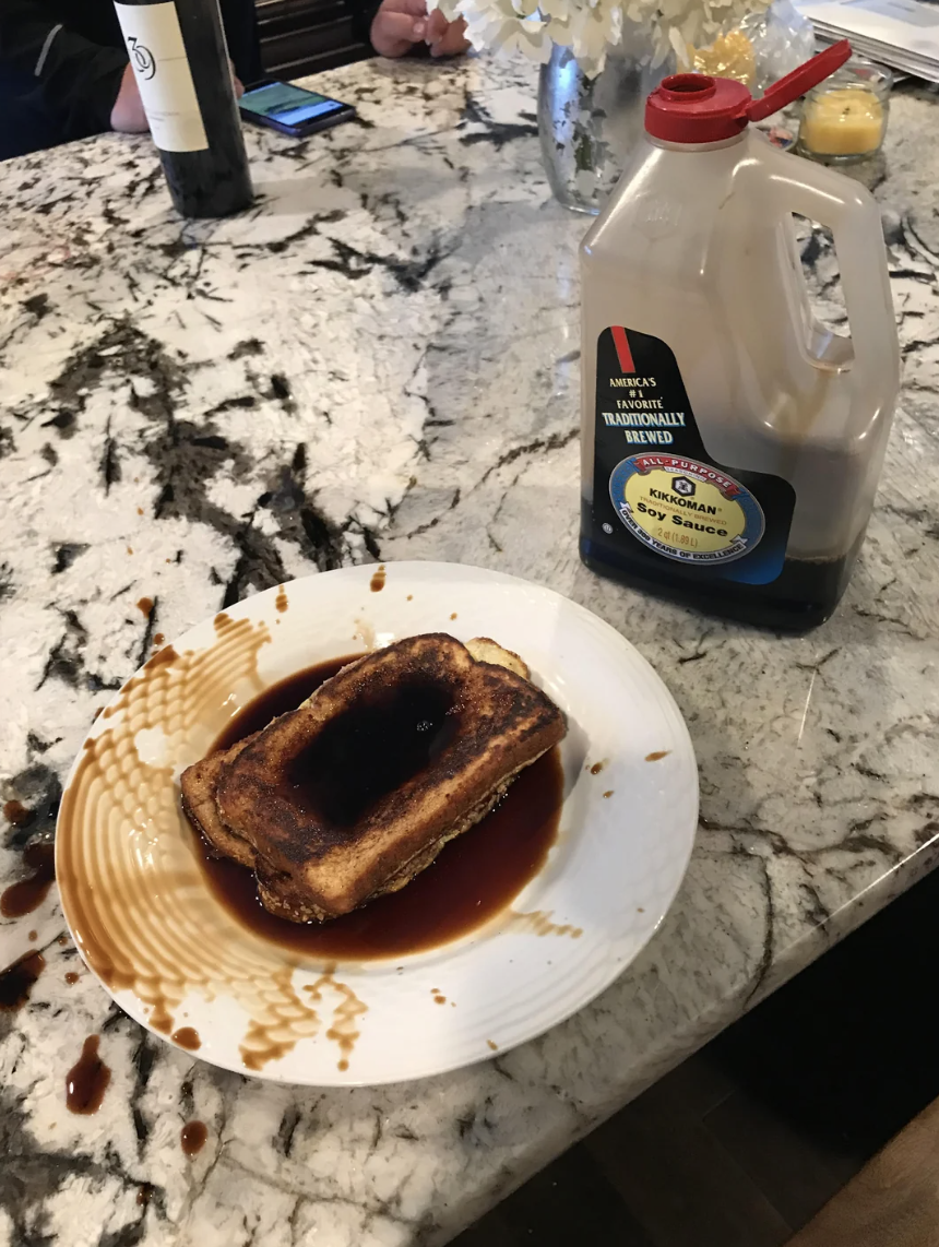 Burnt toast on a plate with an excessive amount of syrup spilling over, next to syrup bottle on a counter