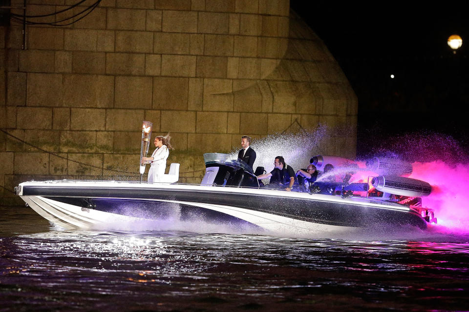 David Beckham passes under Tower Bridge driving a speedboat named 'Max Power' which carries the Olympic Torch with its torchbearer on July 27, 2012 in London, England. Athletes, heads of state and dignitaries from around the world have gathered in the Olympic Stadium for the opening ceremony of the 30th Olympiad. London plays host to the 2012 Olympic Games which will see 26 sports contested by 10,500 athletes over 17 days of competition. (Photo by Matthew Lloyd/Getty Images)