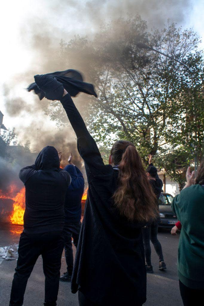 Una mujer sin hiyab junto a otros manifestantes  protesters gathers around burning dumpsters during a protest. The nationwide protests started after the death of Mahsa Amini, a 22-year-old girl who died under the custody of the Islamic Republic's Morality Police on September 16th, 2022 in Tehran, Iran. 