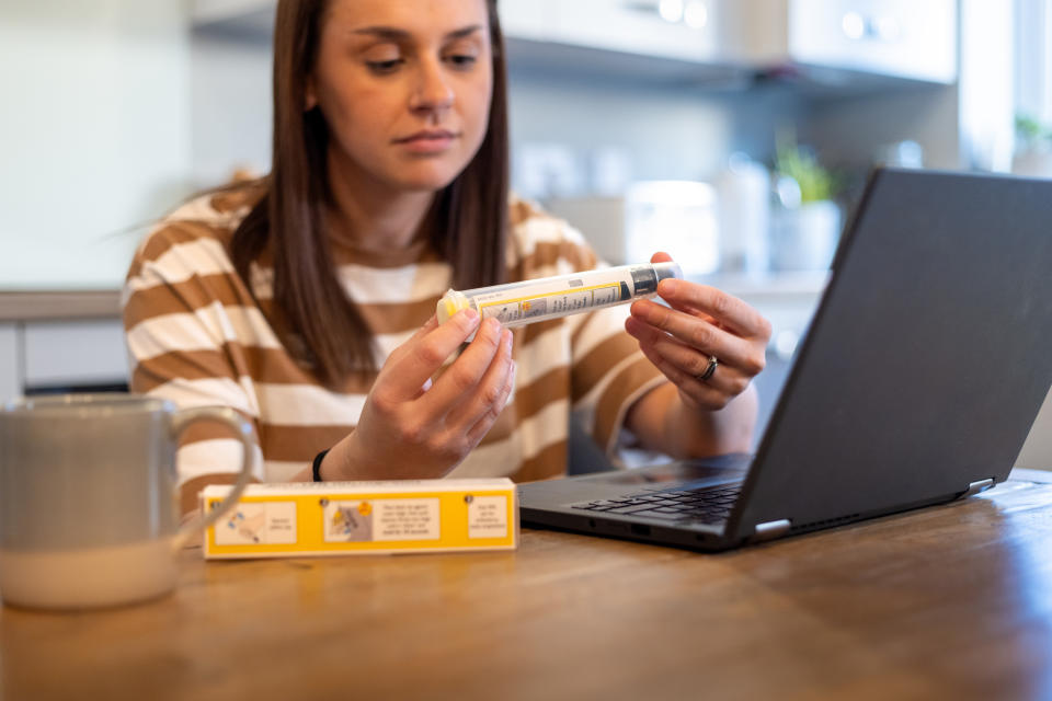 A medium shot of a woman displaying her EpiPen during an online doctor's consultation. She is wearing casual clothing, in the kitchen of her home located in Newcastle Upon Tyne.

Videos are available similar to this scenario.