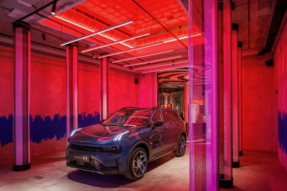 Bold red and purple lighting shines down on Lynk & Co's stylish, smart 01 hybrid vehicle at the company's Milan club.